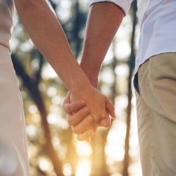 A couple holding hands in the forest.