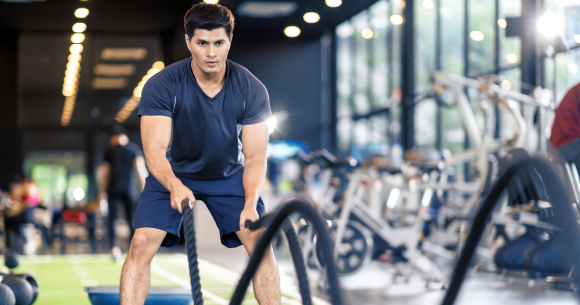 A man in the gym using gym ropes to workout.