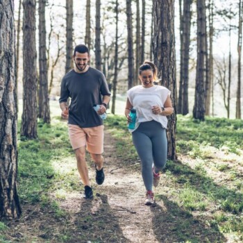 A man and woman running through the forest on a trail.