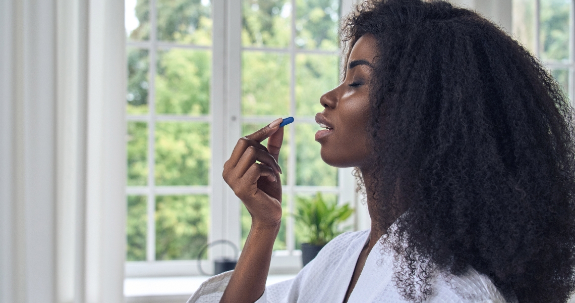 A woman holding a blue pill to her mouth about to take it.