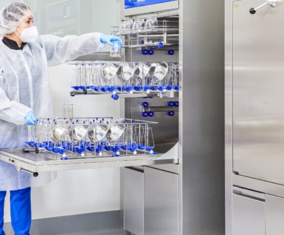 A person in full PPE loading a metal bowl on a rack into sterilizing equipment.