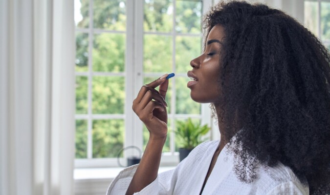 A woman holding a blue pill to her mouth about to take it.