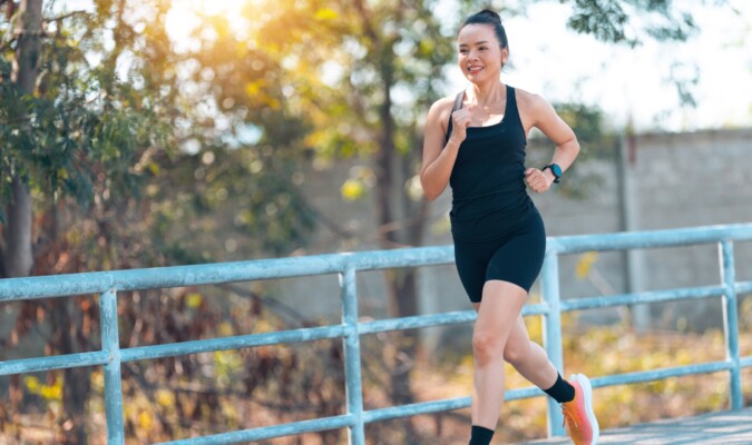 A woman in black workout attire running outdoors.