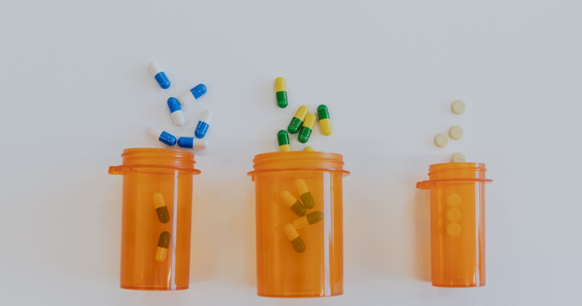 Three orange bottles with different colored capsules spilling out of them on a white background.