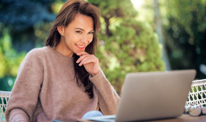 A middle-aged woman with brown hair using her laptop outdoors.