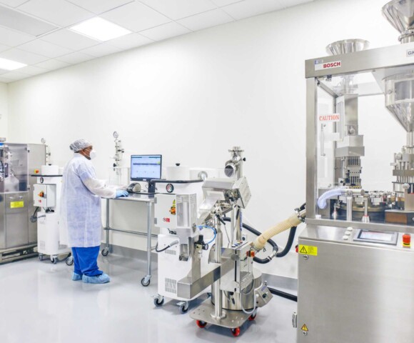 A person in protective clothing using a computer between two pieces of equipment.